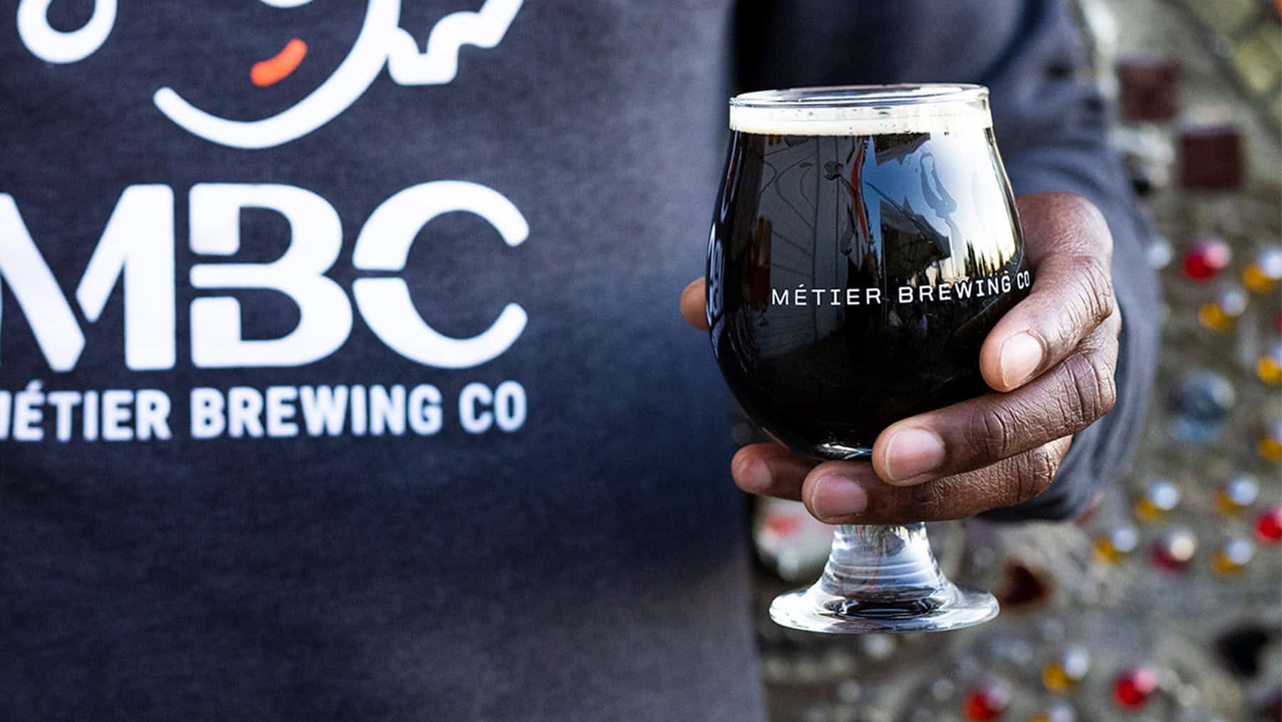 Close-up of hand holding a short glass of dark beer