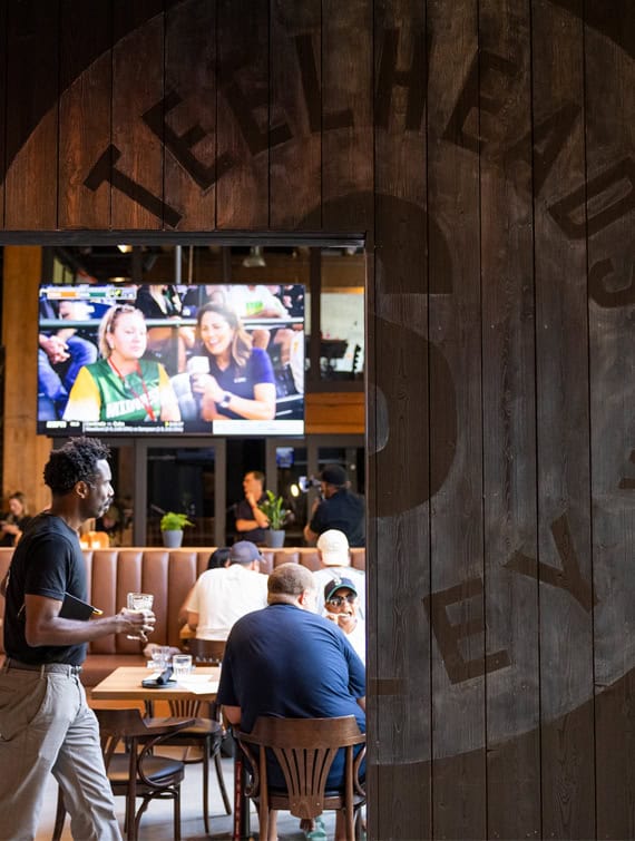 An open doorway looking into the Steelheads bar with customers and a television with a game on.