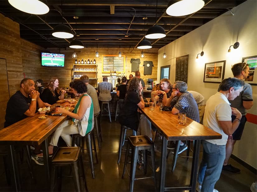 Woodinville room filled with customers at two long tables and a bar.