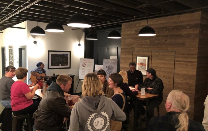 A room full of customers listening to a person playing guitar and talking to each other.