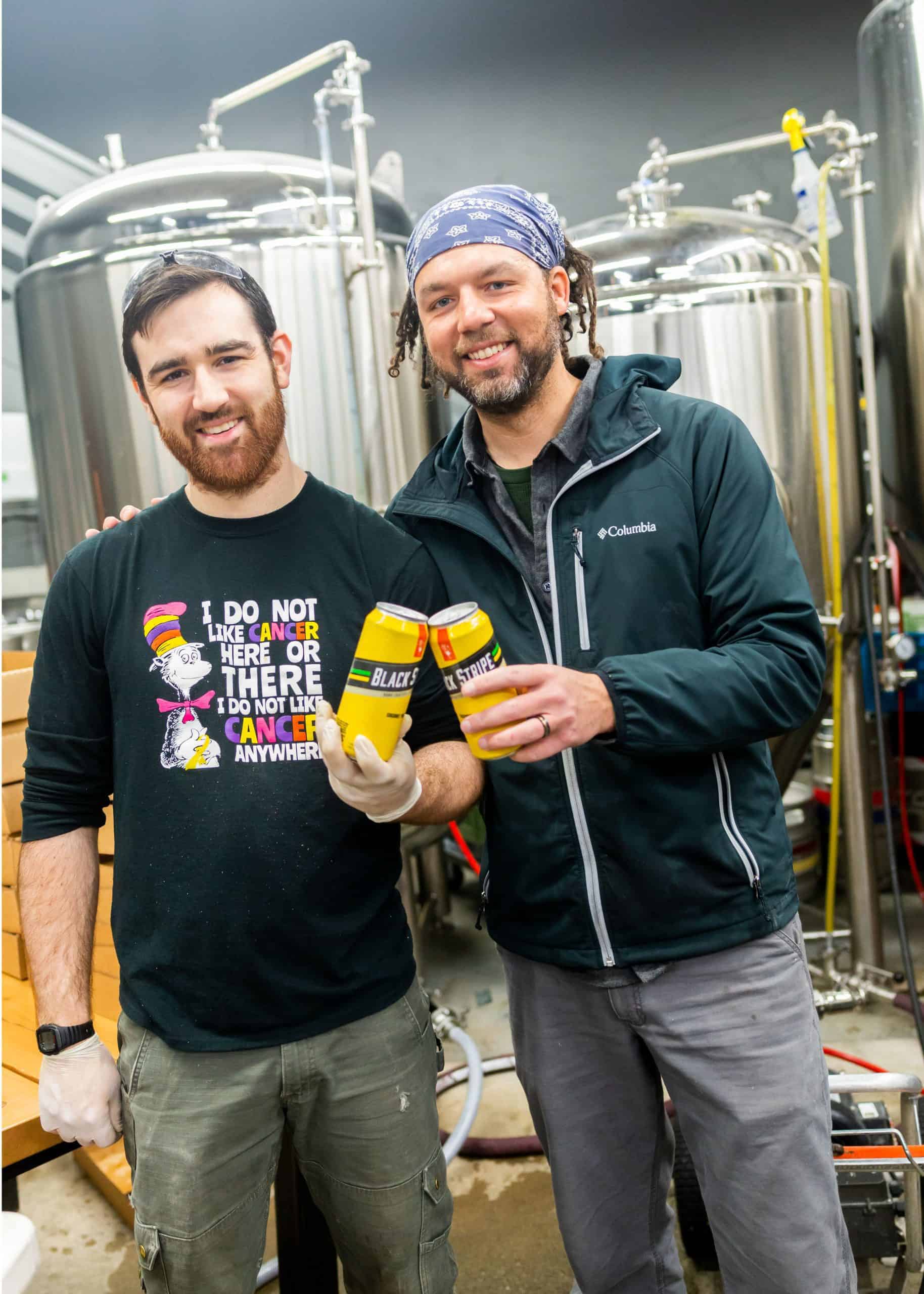 Two people smiling at the camera and holding and touching two Black Stripe cans together